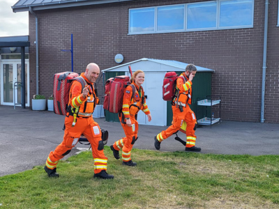 Critical care paramedics Dan Tucker and Sophie with Dr Reuben Cooper wearing flight suits and red kit bags.